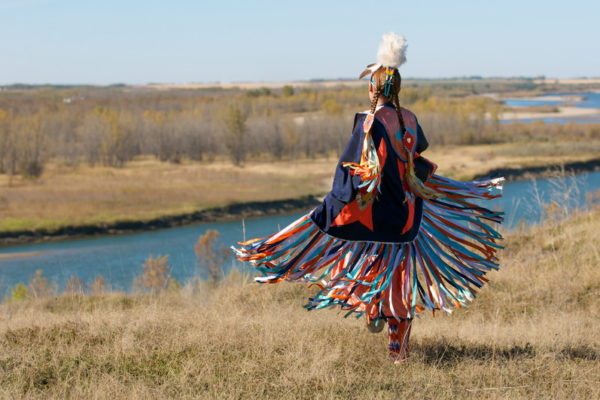 First Nation dancer in traditional attire near a river